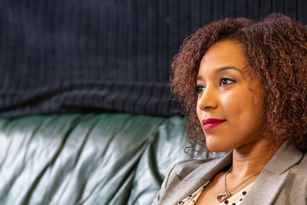 Mujer negra sonriente con mirada reflexiva pensativa contra fondo oscuro con espacio de copia para su texto o contenido publicitario