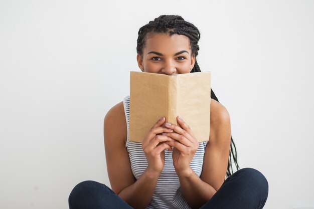 Mujer negra sonriente que se oculta detrás del libro abierto