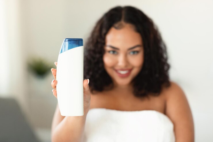Mujer negra sonriente de talla grande que muestra una botella de champú vacía con una maqueta para el diseño en el enfoque selectivo de la cámara