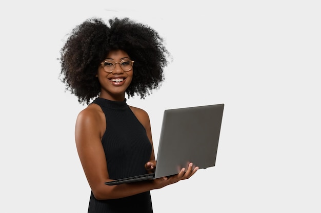 mujer negra sosteniendo una computadora mientras mira y sonríe a la pantalla de la computadora con fondo blanco