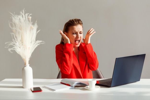 Foto mujer nerviosa en traje rojo está gritando mirando el monitor de la computadora portátil mujer estresada en el trabajo