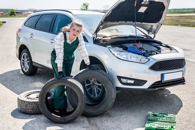 Foto mujer con neumáticos en la carretera con coche roto