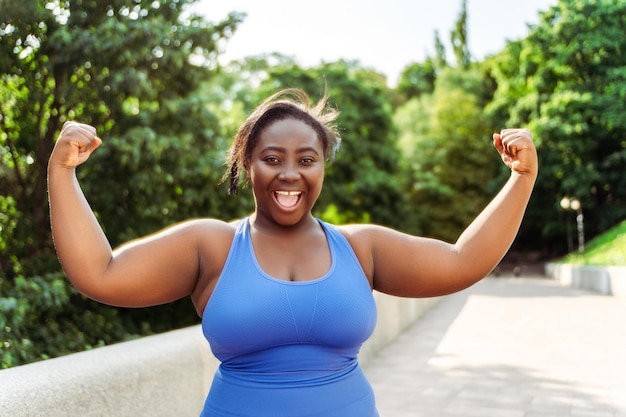 Mujer nigeriana sonriente positiva vistiendo ropa deportiva mostrando bíceps mirando a la cámara