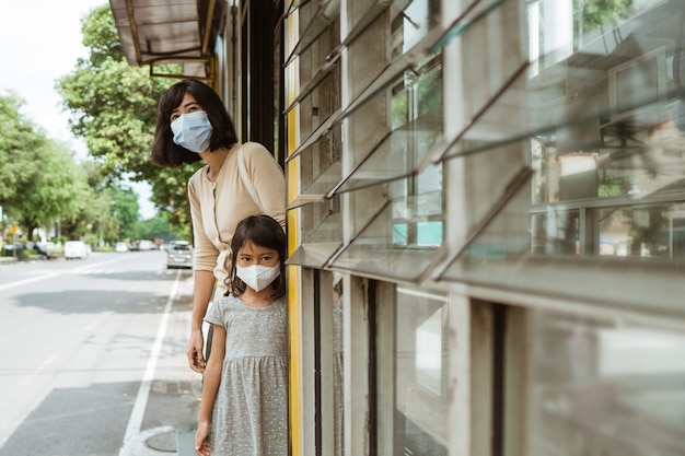 Una mujer y una niña con una máscara está esperando el autobús en la parada de autobús
