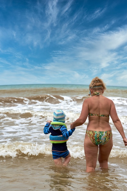 Una mujer y un niño caminan hacia el mar tomados de la mano, vista desde atrás