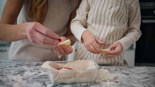 Mujer niño manos poniendo manzana en forma de hornear de cerca Familia preparando pastel