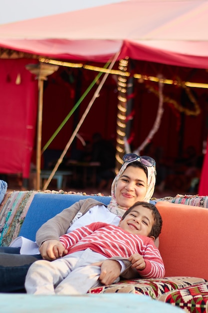 Una mujer y un niño se sientan en un sofá frente a una carpa roja.