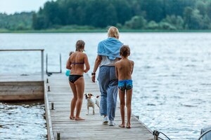 Foto una mujer con niños y un perro camina por un muelle de madera hasta el lago