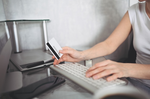 Mujer no reconocida con tarjeta de crédito en la mano y usando el teclado de la computadora portátil. Empresaria o empresario trabajando. Compras en línea, comercio electrónico, banca por Internet, concepto de gasto de dinero