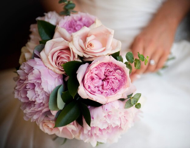 Una mujer una novia sosteniendo un ramo de novia de rosas de color rosa pálido y peonías de lavanda