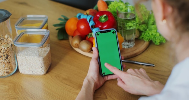 Mujer nutricionista con frutas y verduras saludables usando un teléfono inteligente con pantalla verde Pantalla verde fácil de personalizar Concepto correcto de nutrición y dieta