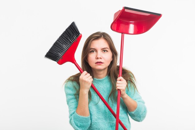 Mujer o ama de casa sosteniendo una escoba, cansada de limpiar, en la pared blanca, aislada con espacio de copia.