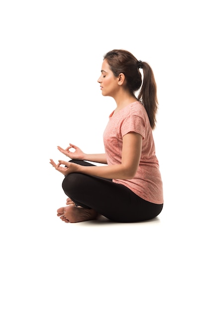 Foto mujer o niña india que realiza asanas de yoga o meditación o dhyana sentado aislado sobre fondo blanco.