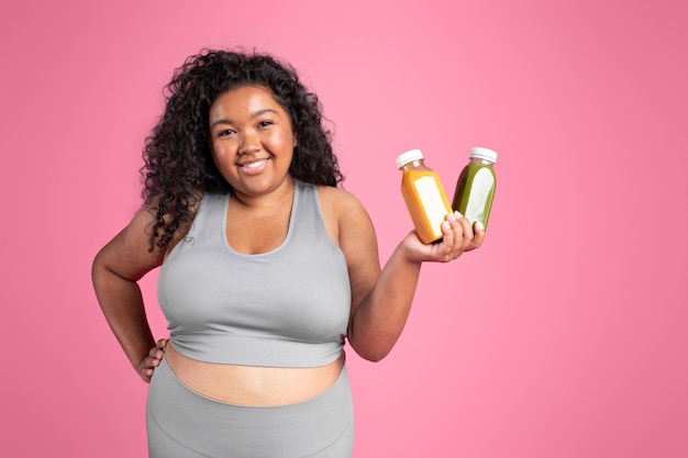 Mujer obesa negra sonriente en ropa deportiva muestra botellas con jugo o recomendación de bebida de batido para