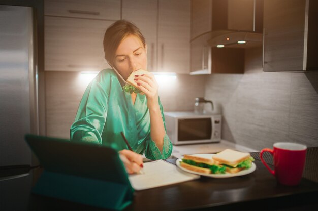 Foto mujer ocupada comiendo, bebiendo café, hablando por teléfono, trabajando en la computadora portátil al mismo tiempo. la empresaria realizando múltiples tareas