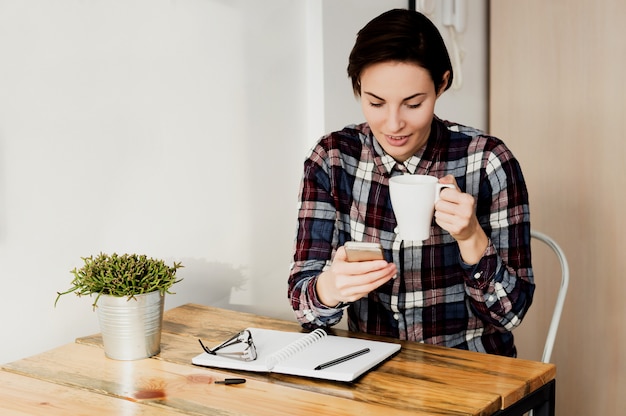 Mujer ocupada en la oficina en casa usando el teléfono y tomando café.