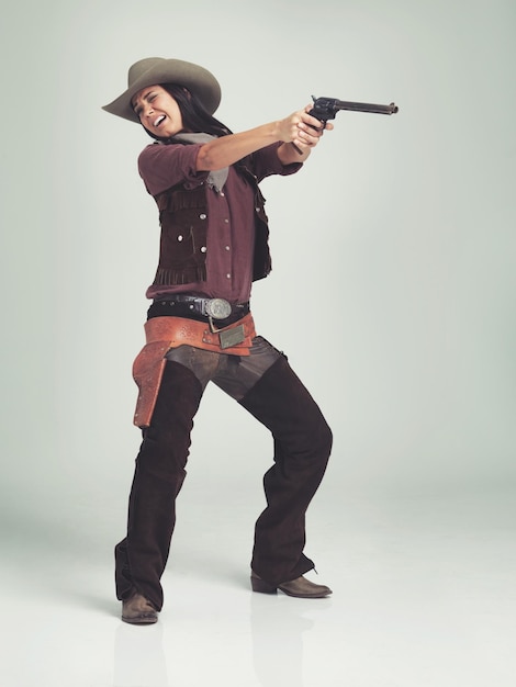 Mujer del oeste y vaquero con arma en el estudio para la moda nerviosa y asustada de disparar en fondo gris Persona femenina vintage y fuera de la ley con pistola para el traje del oeste salvaje y personaje con sombrero