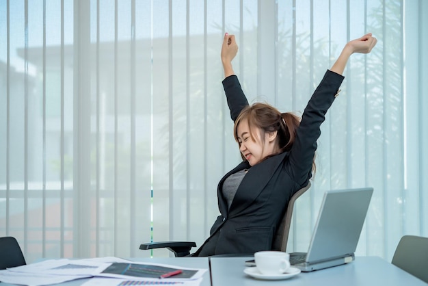 Mujer oficial asiática estirando el cuerpo en el escritorio de la oficina desde el ángulo posteriorGente de TailandiaEmpresaria cansada del trabajo duro