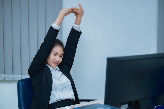 Mujer oficial asiática estirando el cuerpo en el escritorio de la oficina desde el ángulo posteriorGente de TailandiaEmpresaria cansada del trabajo duro