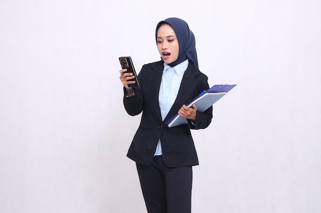 Una mujer de oficina asiática madura con hijab se queda sorprendida mirando y operando un teléfono inteligente y