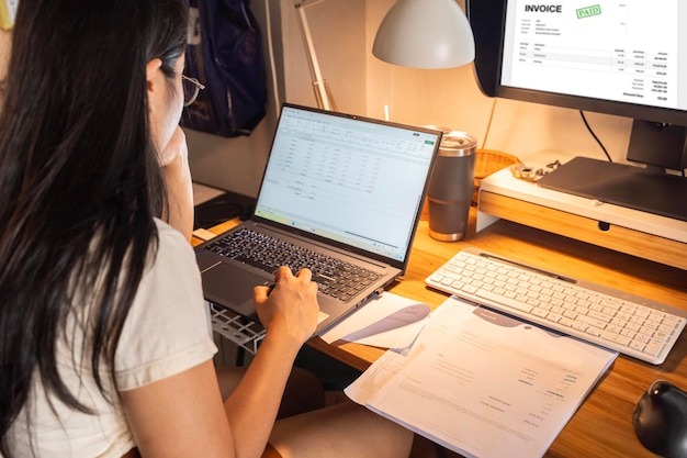 Mujer en la oficina con un ejemplo de documento de factura en la computadora Contadora que utiliza el software Einvoice en la computador en la oficina