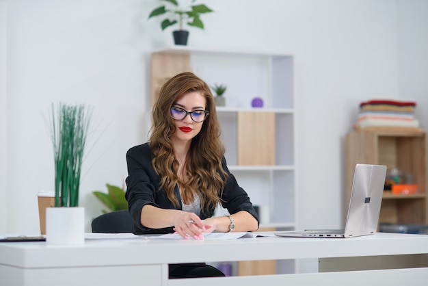 Mujer de oficina joven atractiva en ropa formal trabaja con papeleo comercial en el escritorio.