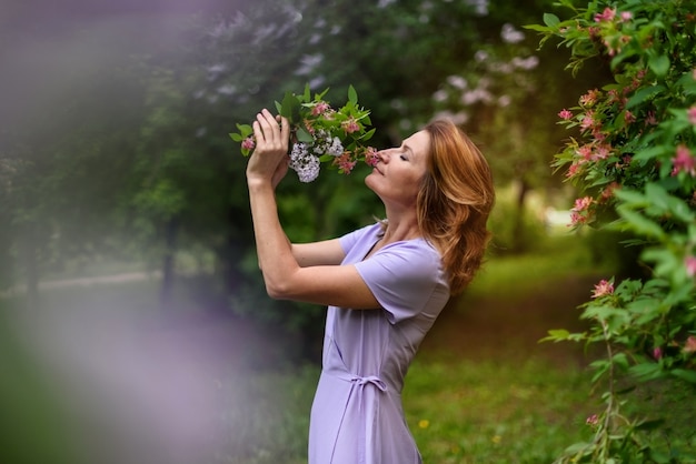 Mujer con los ojos cerrados olfatea un ramo de flores en el parque de verano