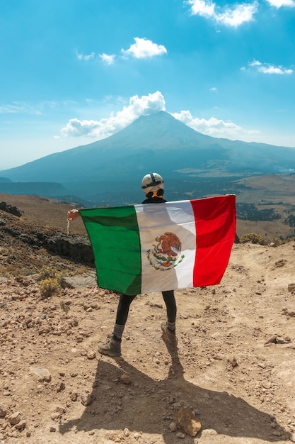 Una mujer ondeando la bandera mexicana en la cima de la montaña