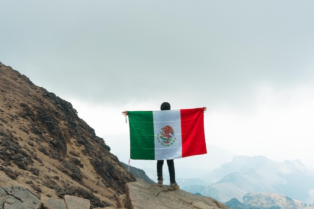 Una mujer ondeando la bandera mexicana en la cima de la montaña