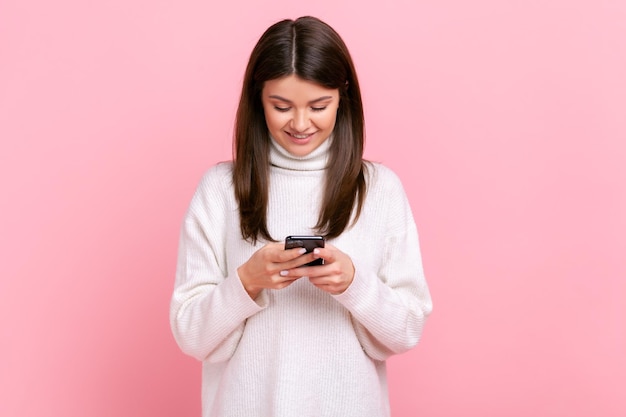 Mujer optimista positiva que usa un teléfono inteligente con expresión facial feliz escuchando noticias agradables