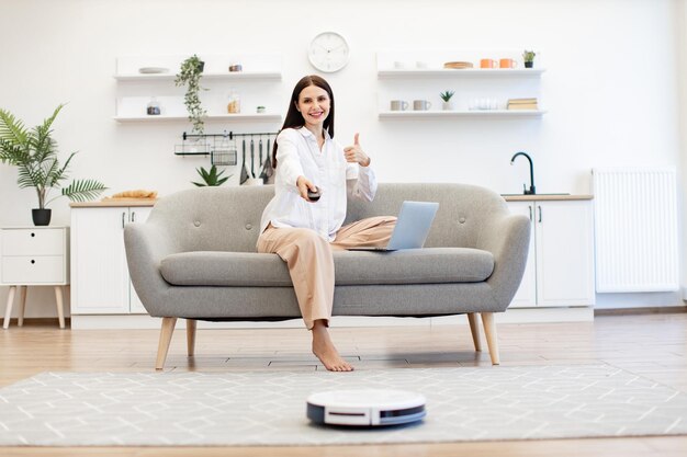 Mujer con ordenador portátil programando limpieza automática del suelo de la habitación