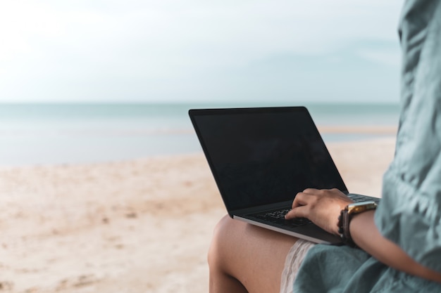 Mujer con ordenador portátil y smartphone para trabajar, estudiar en vacaciones en la playa.