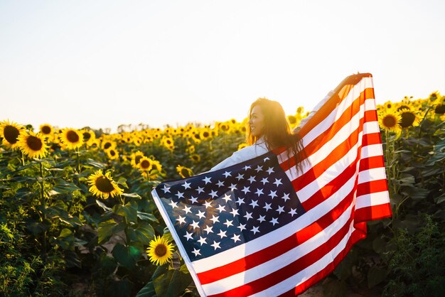 Mujer orgullosamente sostiene ondeando la bandera estadounidense en el campo de girasol Día de la Independencia 4 de julio