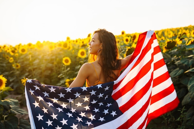 Mujer orgullosamente sostiene ondeando la bandera estadounidense en el campo de girasol Día de la Independencia 4 de julio