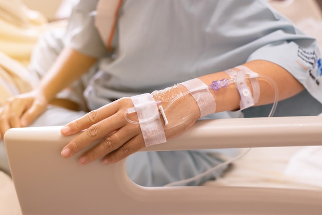 Mujer paciente de manos que recibe solución salina mientras se sienta en la cama enferma en el hospital