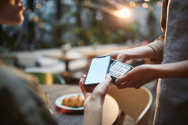 Mujer pagando por teléfono inteligente en café