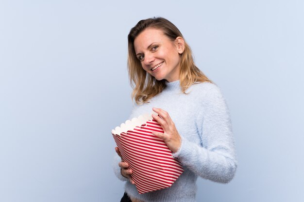 Mujer con palomitas de maíz sobre pared azul aislado