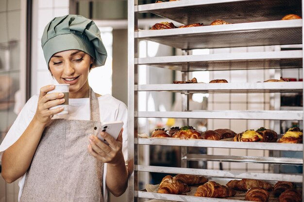 Mujer panadera en la pastelería tomando café y usando el teléfono