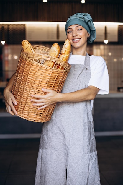 Mujer panadera sosteniendo una cesta llena de baguettes y sonriendo