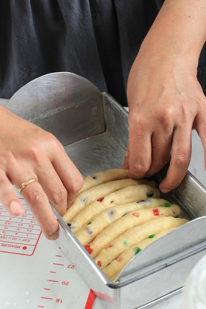 Mujer panadero asiático arreglando la masa de pan crudo con frutos secos en una bandeja para hornear, pan indonesio llamado Roti Sisir o Stollen de Navidad