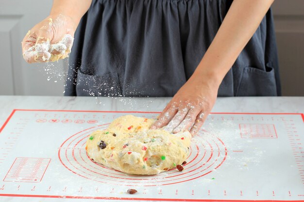 Mujer panadero casero espolvorear harina para evitar masa pegajosa, amasar masa de pan con pasas y frutos secos, proceso de elaboración del pan tradicional alemán Christmast Stollen