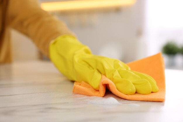 Mujer con un paño de microfibra limpiando una mesa de mármol blanco en el primer plano de la cocina