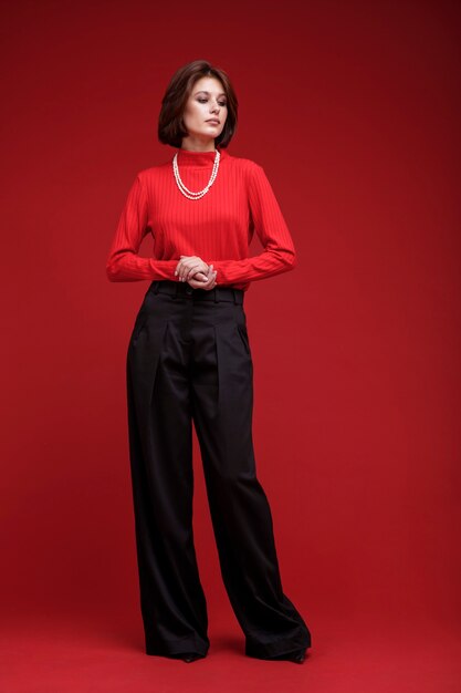 Mujer en pantalón negro collar de perlas superior rojo sobre fondo rojo Corte de pelo Bob Foto de estudio