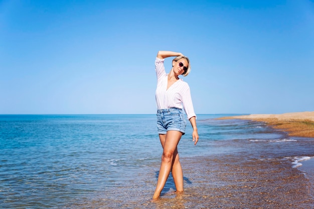 Una mujer en pantalones cortos de vaqueros camina a lo largo de la orilla del agua en una playa de arena Resort de vacaciones de relajación y viajes