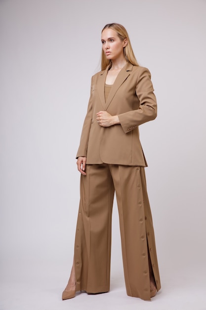 Foto mujer en pantalones de traje marrón beige desabrochado en la costura de la chaqueta fondo blanco foto de estudio