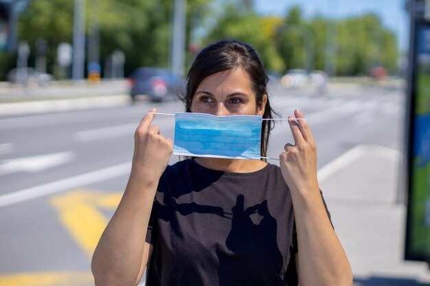 Foto mujer en una parada de autobús poniéndose una máscara en la cara