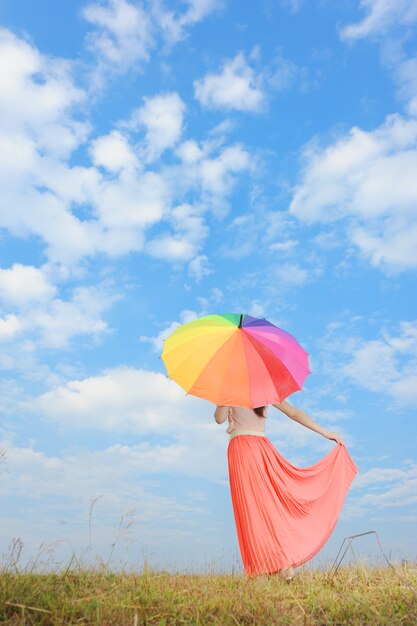 Mujer con paraguas de arco iris y cielo azul