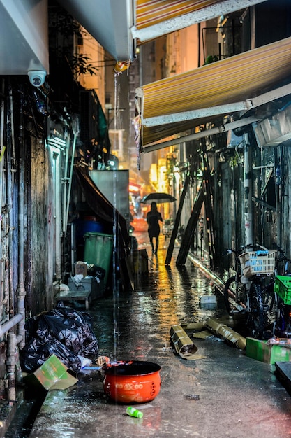 Mujer con paraguas en un callejón en medio de edificios en la ciudad por la noche durante la temporada de lluvias