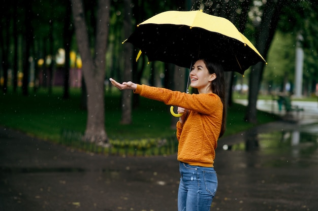 Mujer con paraguas disfruta de la lluvia en el parque de verano, día lluvioso. Persona de sexo femenino caminando solo, clima húmedo en el callejón