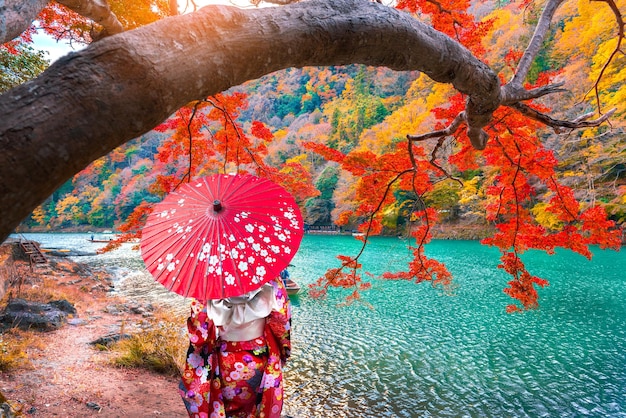 Foto mujer con paraguas de pie junto al río durante el otoño